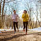 a couple jogs down a dirt path through the snowy forest wearing affordable workout clothes