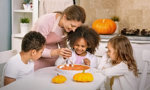 Mom and three children at kitchen table decorating pumpkin dessert for a blog about trader joe's fall recipes