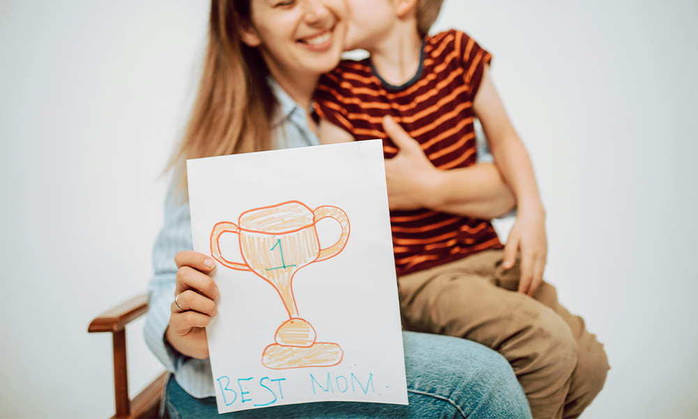 Mom holding toddler son and holding up drawing that says number one mom for a blog highlighting Mother's Day Gift Ideas
